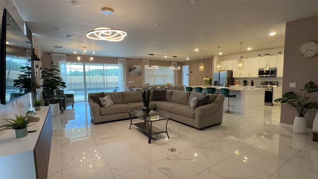 An open-concept living room and kitchen featuring white tile floors and a large sectional sofa — 3820 SONOMA BOULEVARD, KISSIMMEE, FL