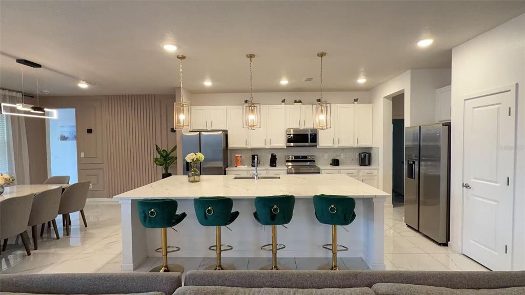 A modern kitchen features a large white island with four green velvet bar stools — 3820 SONOMA BOULEVARD, KISSIMMEE, FL