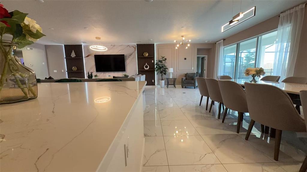 A modern open-concept living and dining area features marble tile floors and a large television — 3820 SONOMA BOULEVARD, KISSIMMEE, FL