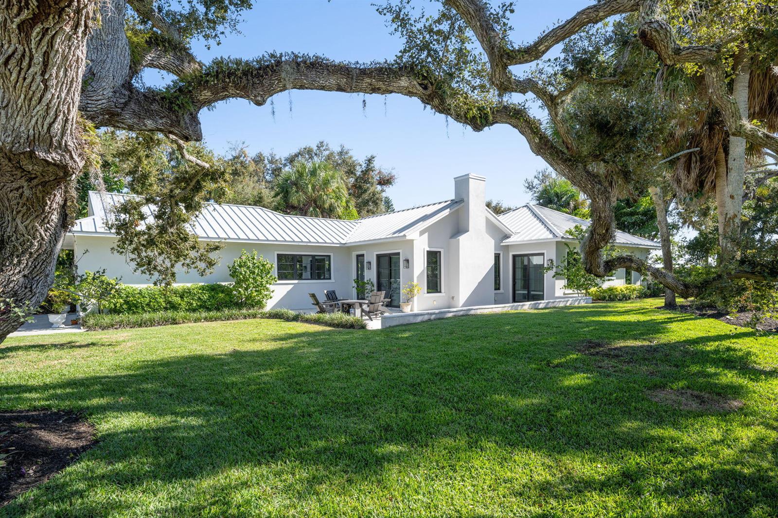 A single-story house with a metal roof sits behind a large tree in a yard — 506 Conn Way, Vero Beach FL 32963, VERO BEACH, FL