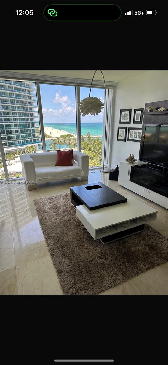 A living room with a white sofa, modern coffee table, and floor-to-ceiling ocean view windows — 10275 Collins Ave # 808, Bal Harbour FL 33154, BAL HARBOUR, FL