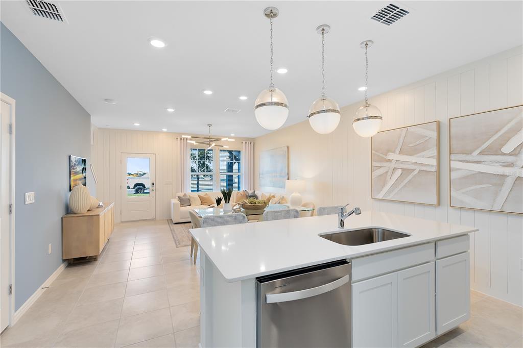 A modern kitchen island with a stainless steel dishwasher overlooks an open-concept living and dining area — 2118 SOUTHBURY DRIVE, KISSIMMEE, FL