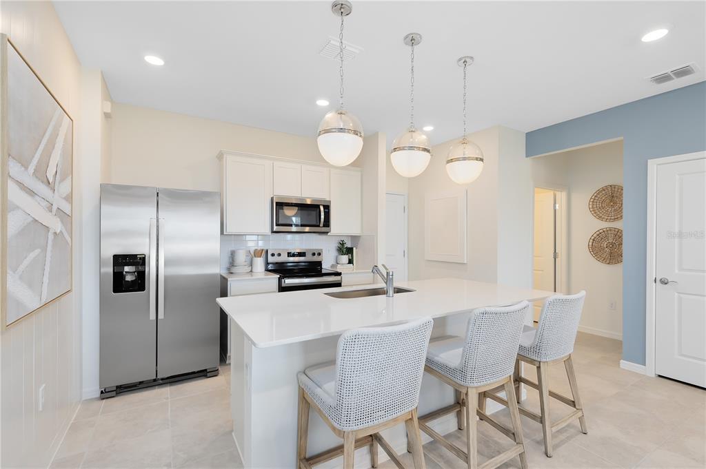A modern kitchen features white cabinets, stainless steel appliances, a quartz island, and three pendant lights — 2118 SOUTHBURY DRIVE, KISSIMMEE, FL