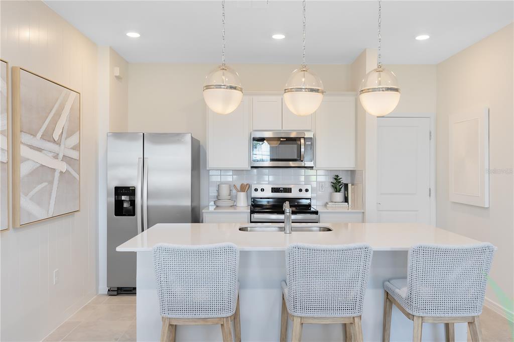A modern kitchen features white cabinets, stainless steel appliances, a quartz island, and three pendants — 2118 SOUTHBURY DRIVE, KISSIMMEE, FL