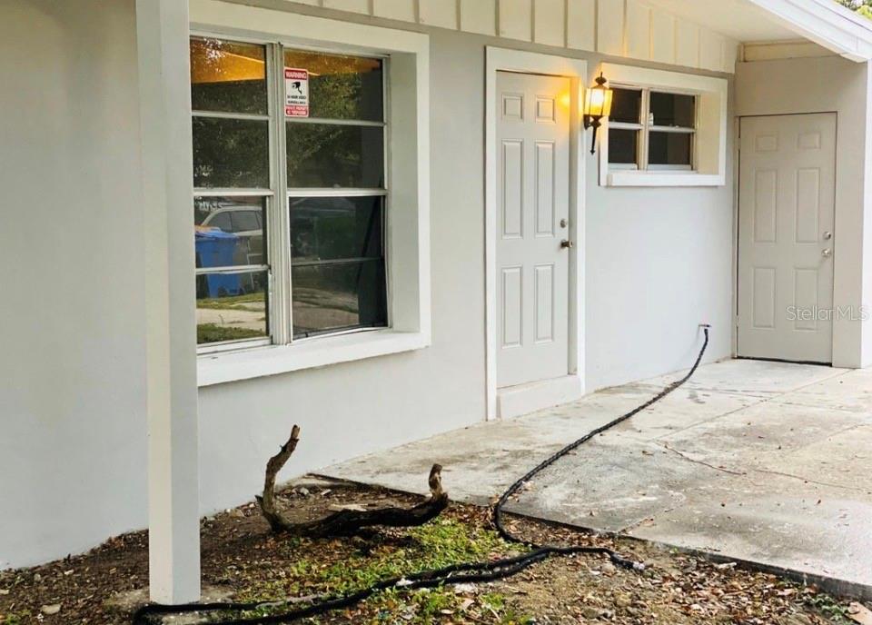 A gray exterior wall features a window, two doors, and a light fixture on a porch — 3207 CLIFFORD SAMPLE DRIVE, TAMPA, FL