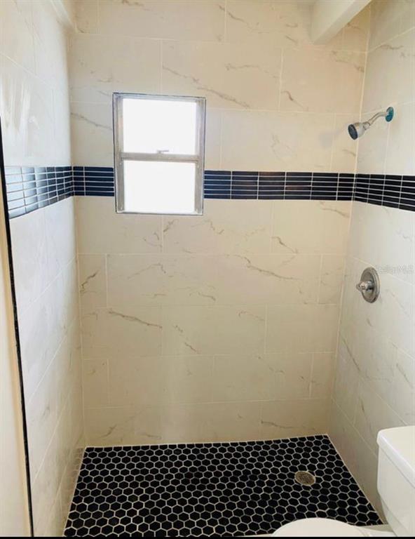 A shower stall features light marble-look wall tiles, a black accent stripe, and hexagonal floor tiles — 3207 CLIFFORD SAMPLE DRIVE, TAMPA, FL