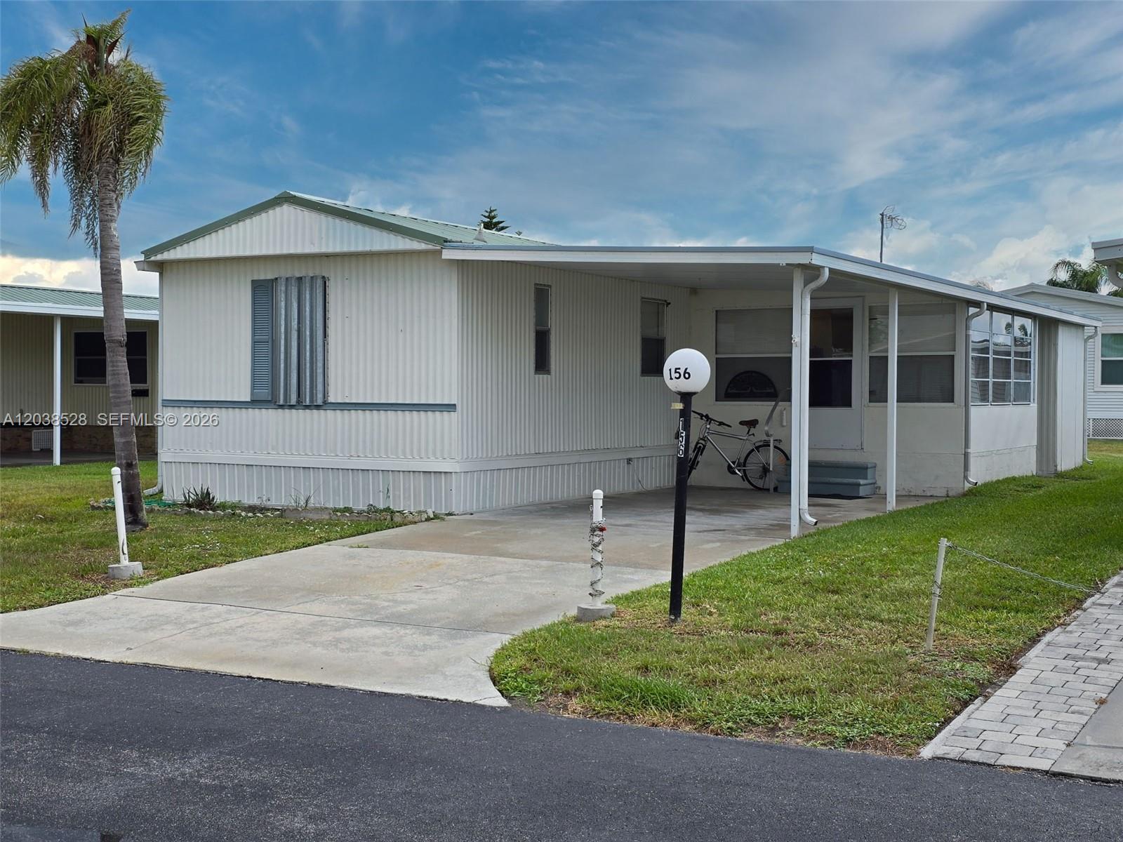 A single-story mobile home with a carport, a palm tree, and a paved driveway — 1601 US HWY 441 SE #156, Okeechobee FL 34974, OKEECHOBEE, FL