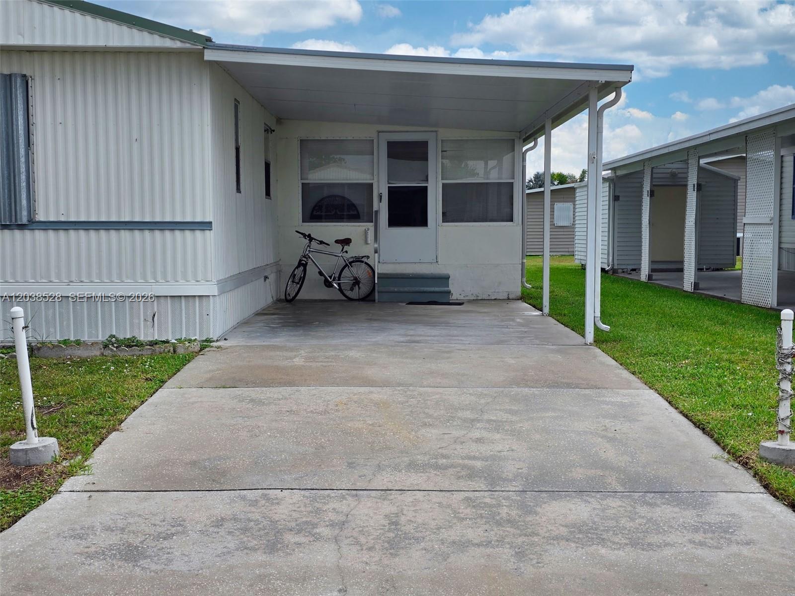 A mobile home exterior features a concrete driveway, a covered carport, and a bicycle — 1601 US HWY 441 SE #156, Okeechobee FL 34974, OKEECHOBEE, FL