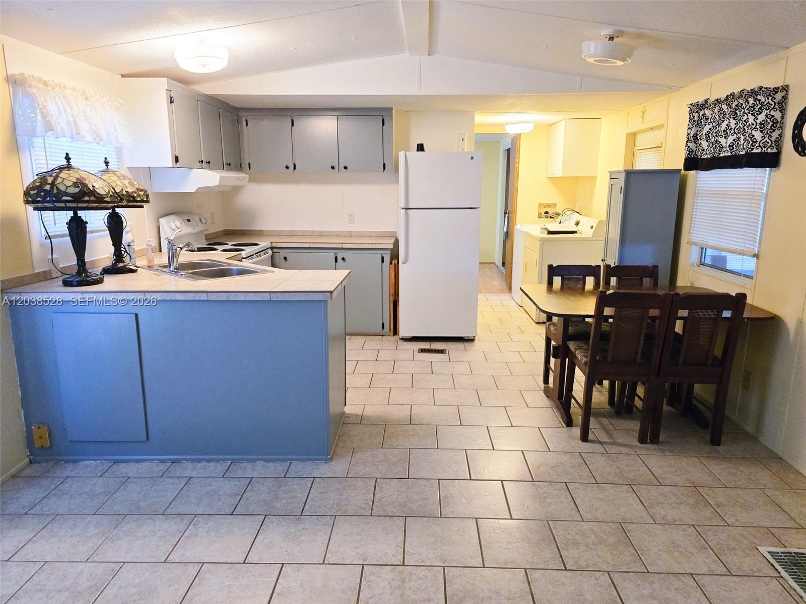 A kitchen with blue cabinets, tile countertops, a white refrigerator, and a dining area — 1601 US HWY 441 SE #156, Okeechobee FL 34974, OKEECHOBEE, FL