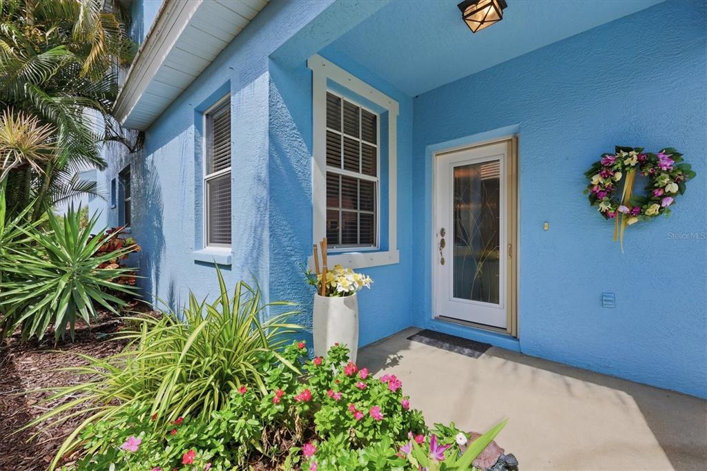 A bright blue house exterior features a front door, a window, and a flower garden — 3271 OSPREY LANE, PORT CHARLOTTE, FL