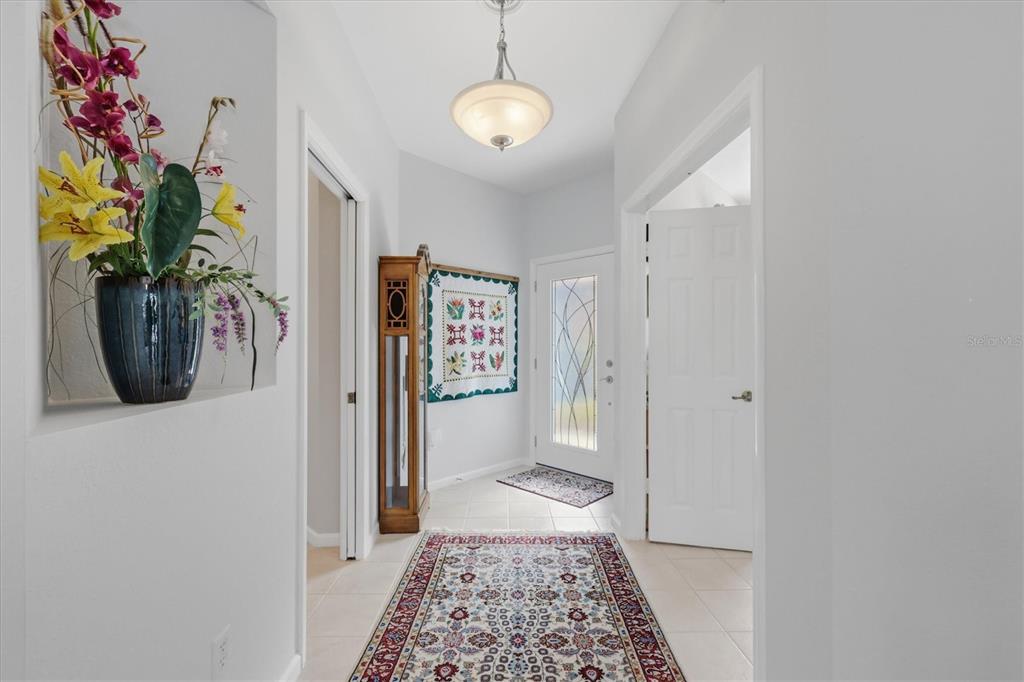 A bright entryway features a patterned rug, a grandfather clock, and a decorative wall quilt — 3271 OSPREY LANE, PORT CHARLOTTE, FL