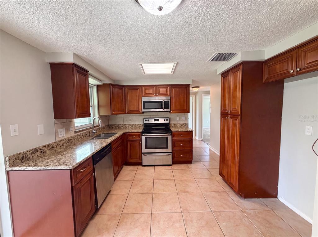 A kitchen features wood cabinets, granite countertops, stainless steel appliances, and light-colored tile flooring — 3412 NIXON ROAD, HOLIDAY, FL