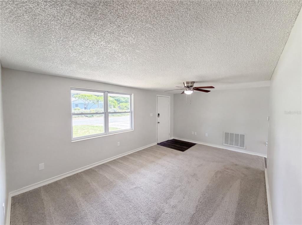 A living room with gray carpet, light gray walls, a ceiling fan, and a window — 3412 NIXON ROAD, HOLIDAY, FL