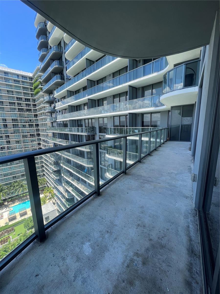 A high-rise balcony with a concrete floor and glass railings overlooks a swimming pool area — 121 NE 34 St # 2215, Miami FL 33137, MIAMI, FL