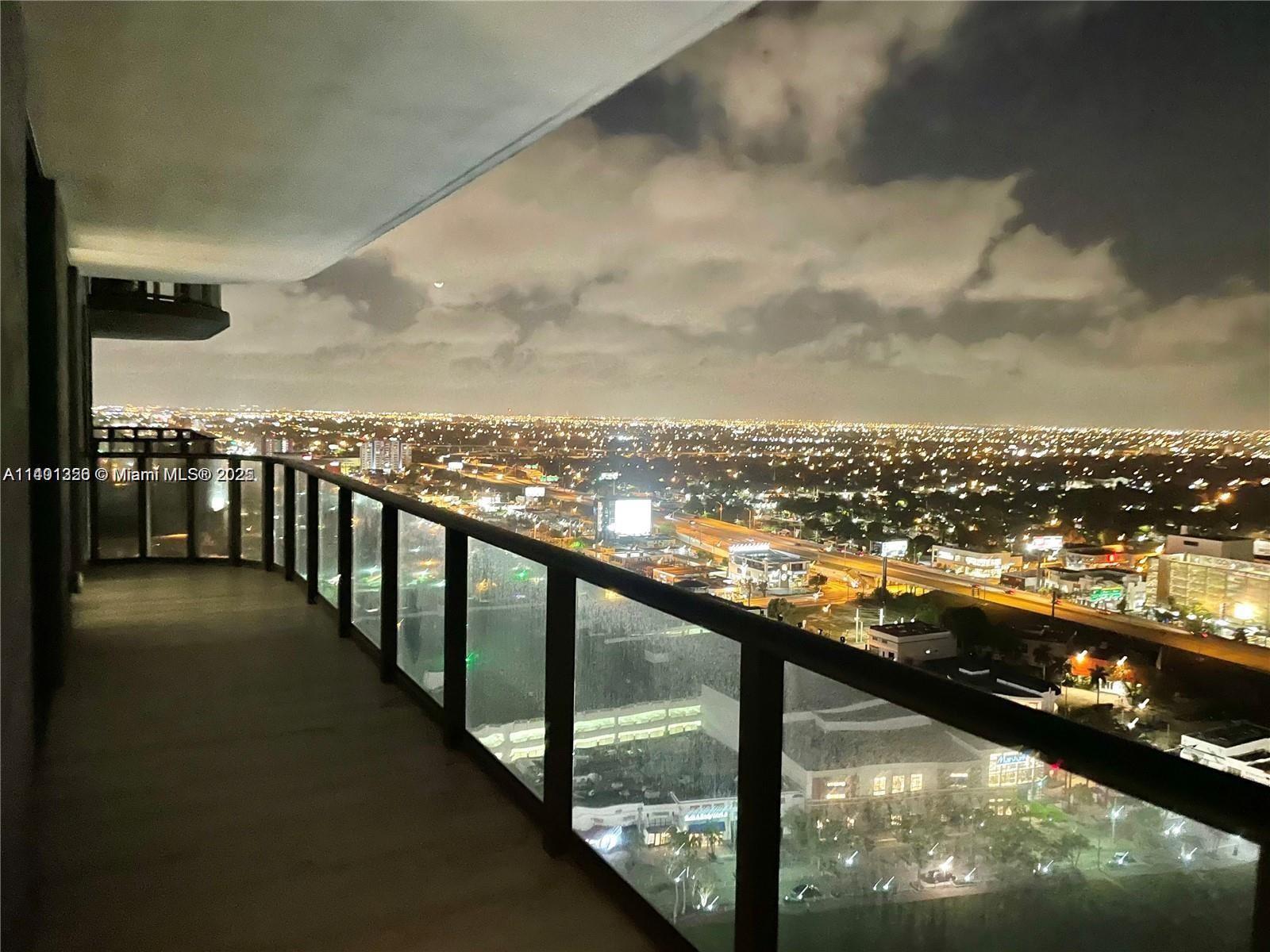 A high-rise balcony at night overlooks a sprawling city landscape with illuminated streets and buildings — 121 NE 34 St # 2215, Miami FL 33137, MIAMI, FL