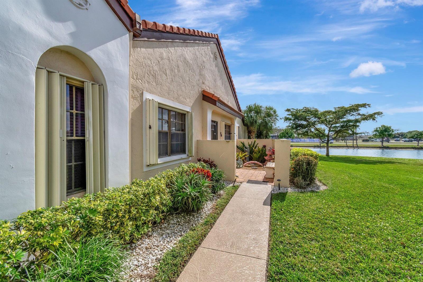 A sidewalk leads to the entrance of a tan stucco home beside a small lake — 8240 Waterline Drive, Boynton Beach FL 33472, BOYNTON BEACH, FL