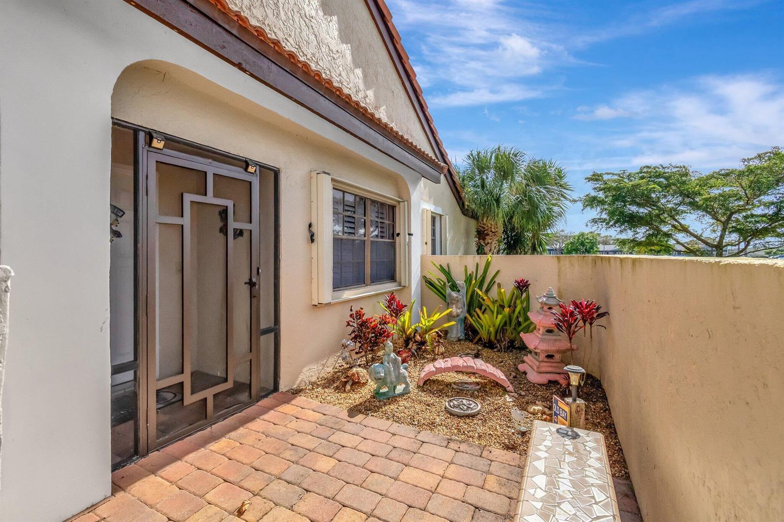 A paved patio area features a decorative garden with a small bridge and stone ornaments — 8240 Waterline Drive, Boynton Beach FL 33472, BOYNTON BEACH, FL