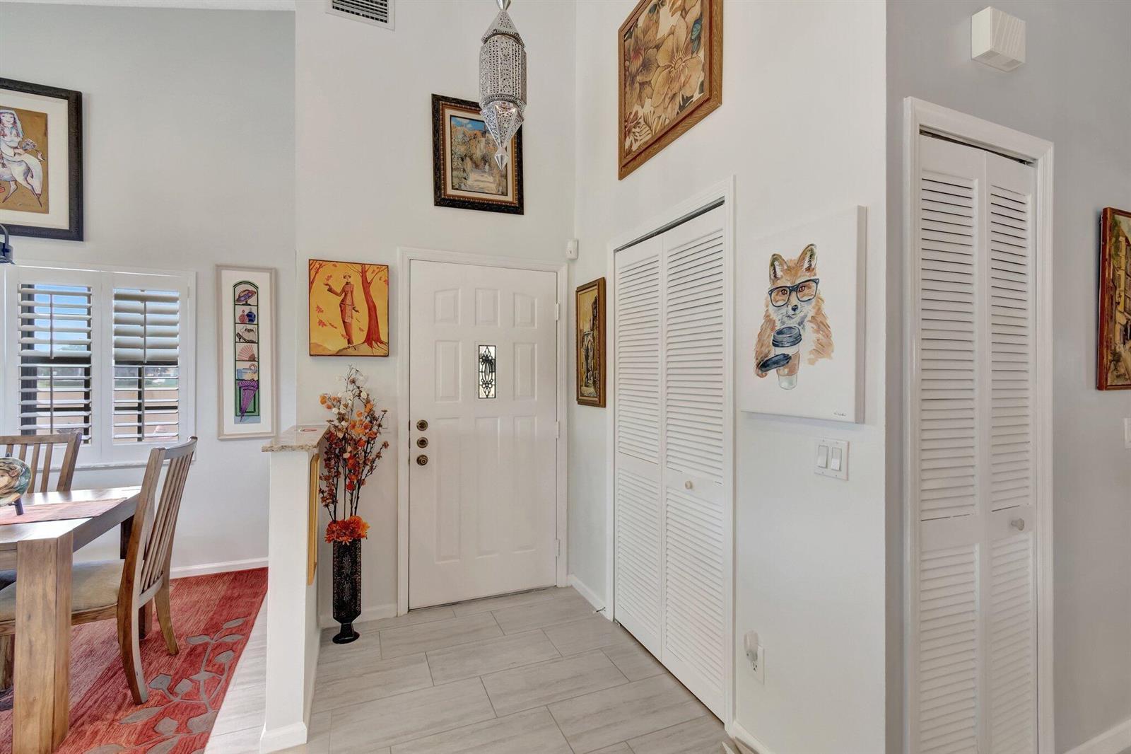 An entryway features a white door, louvered closets, tiled floors, and various wall art pieces — 8240 Waterline Drive, Boynton Beach FL 33472, BOYNTON BEACH, FL