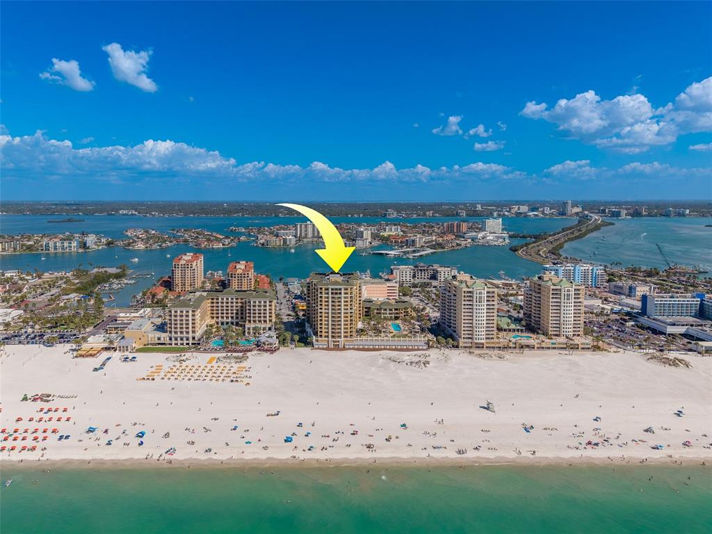 An aerial view of a beachfront high-rise building on a sandy shore with water nearby — 11 BAYMONT STREET UNIT 1109, CLEARWATER BEACH, FL