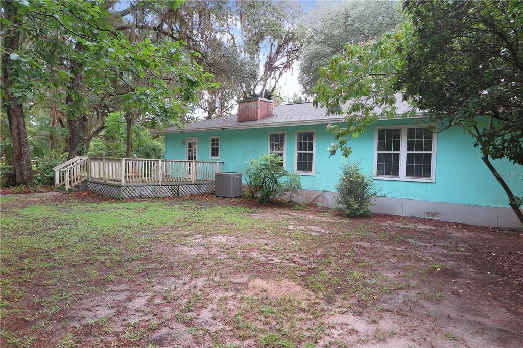 A teal, single-story house features a wooden deck, a brick chimney, and a grassy yard — 11519 SE 225TH DRIVE, HAWTHORNE, FL