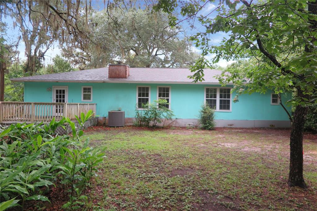 A teal, single-story house with a wooden deck and a chimney in a wooded yard — 11519 SE 225TH DRIVE, HAWTHORNE, FL