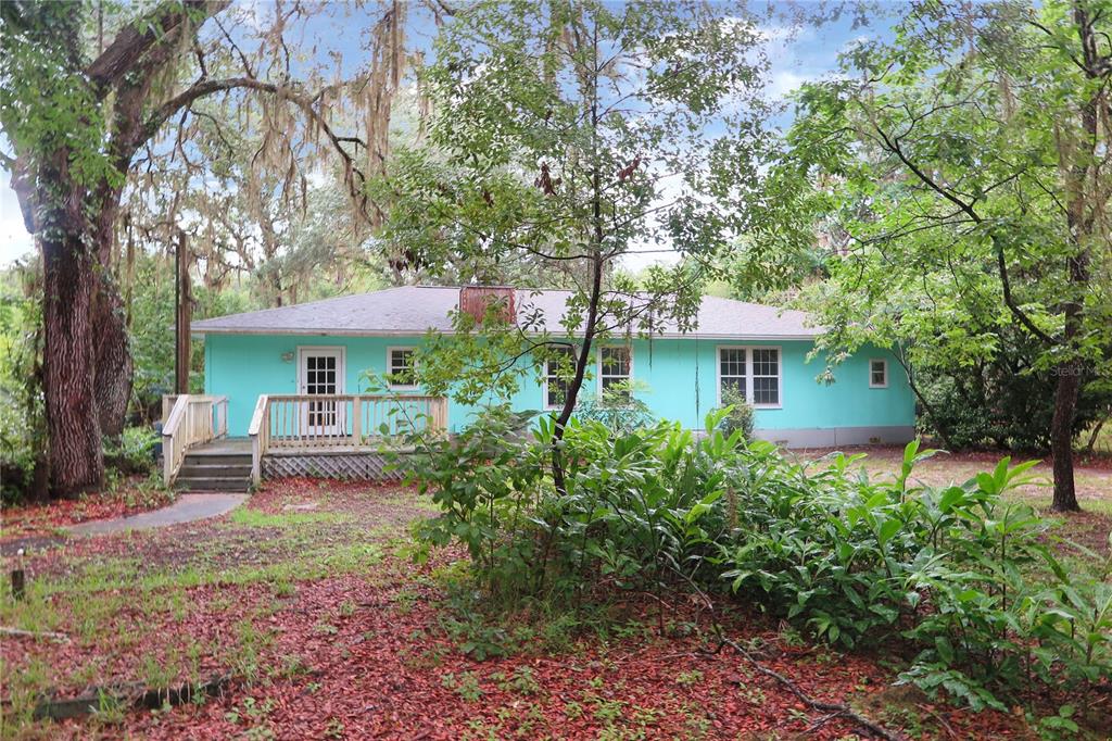 A teal, single-story house with a wooden deck sits among trees and fallen leaves — 11519 SE 225TH DRIVE, HAWTHORNE, FL