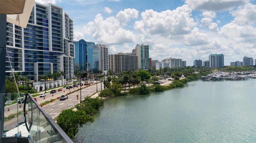 An elevated view shows a coastal city street, high-rise buildings, and a marina with boats — 688 GOLDEN GATE POINT UNIT 302, SARASOTA, FL