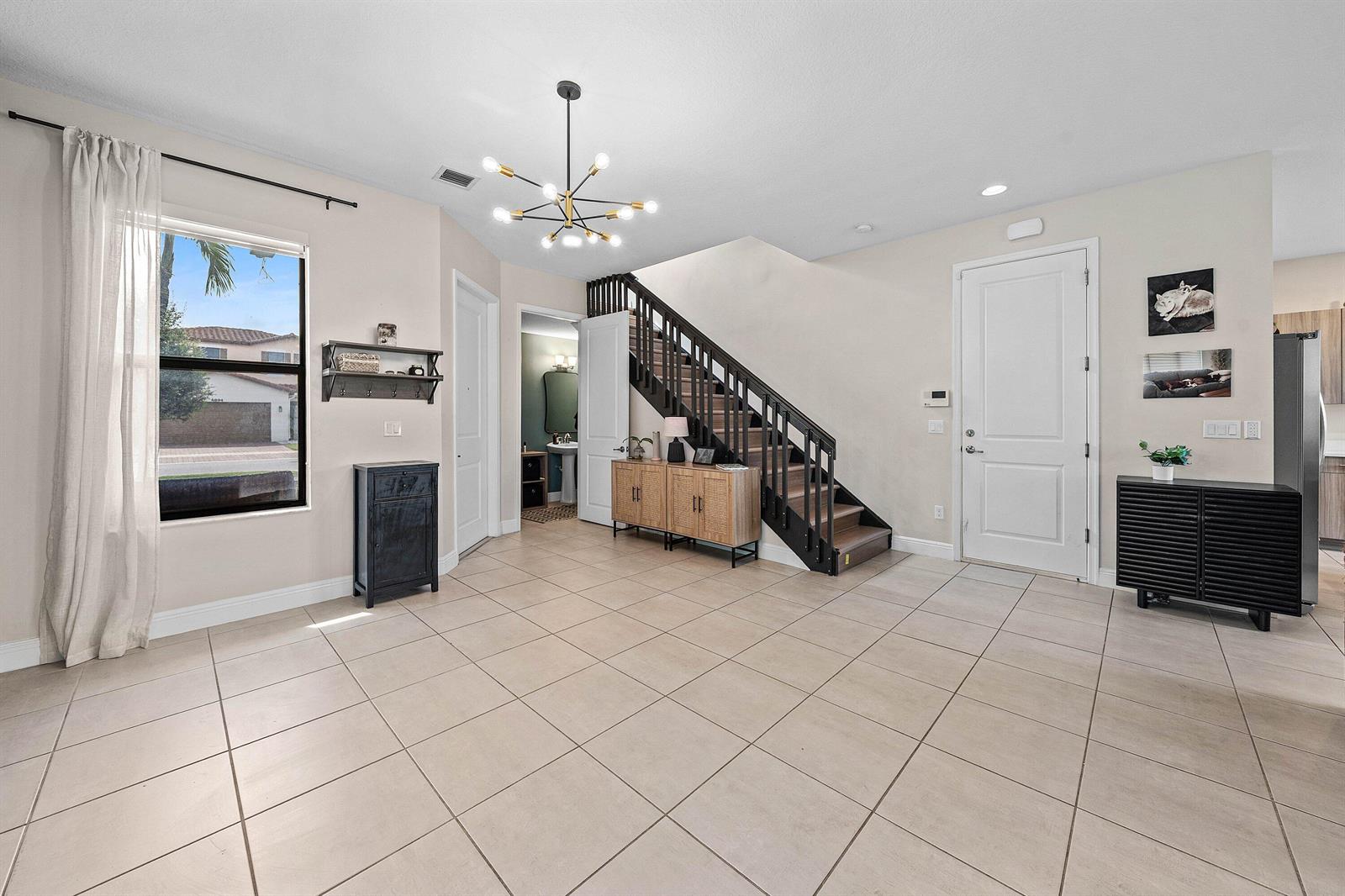 An entryway features tile flooring, a staircase with black railings, and a modern chandelier — 4895 Sand Dollar Drive, Westlake FL 33470, WESTLAKE, FL