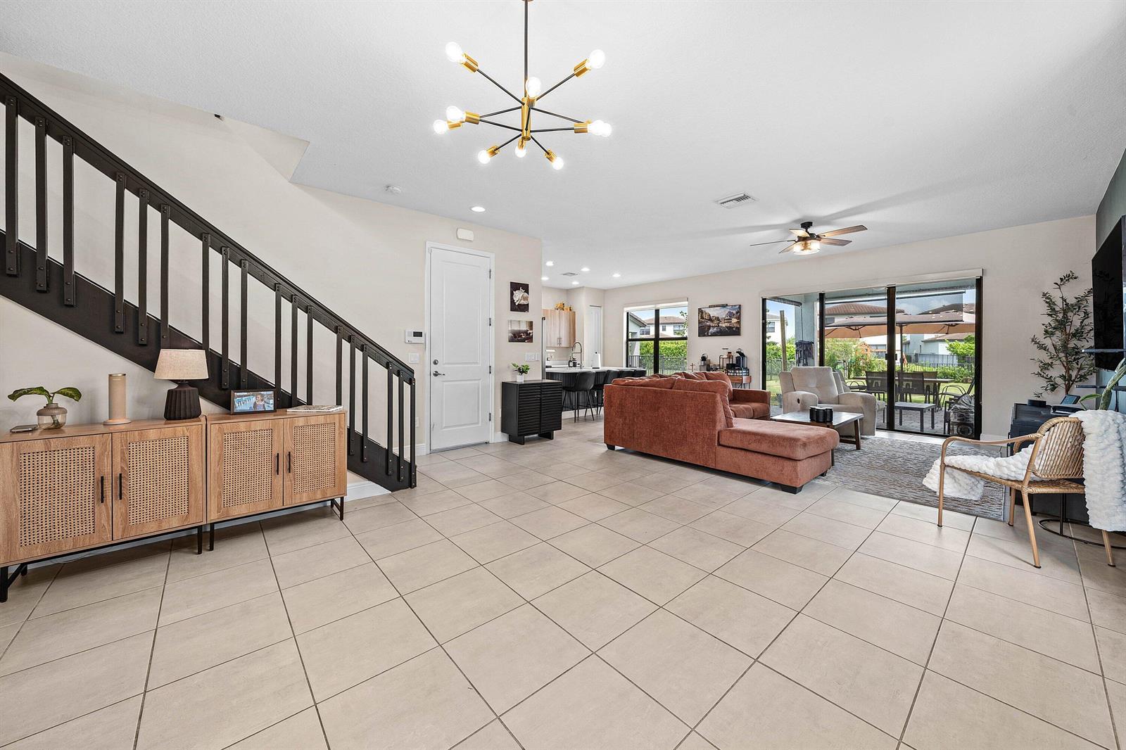 A spacious open-concept living room features tile flooring, a staircase, and a modern chandelier — 4895 Sand Dollar Drive, Westlake FL 33470, WESTLAKE, FL