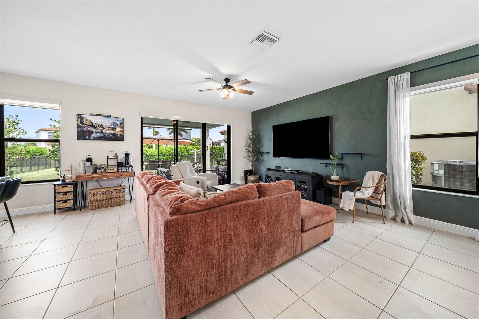 A living room features a large rust-colored sectional, a dark green accent wall, and tile flooring — 4895 Sand Dollar Drive, Westlake FL 33470, WESTLAKE, FL