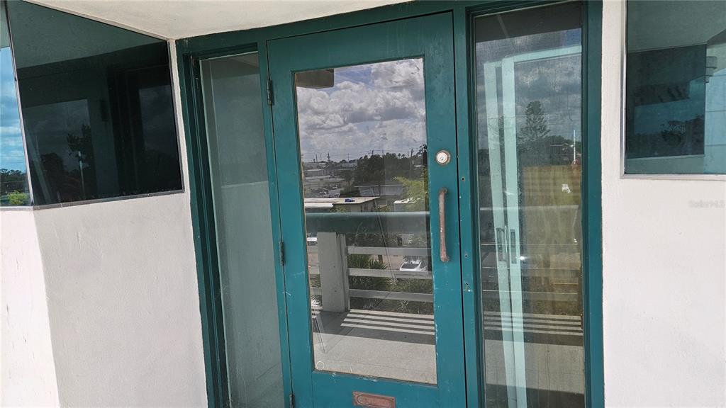 A teal-framed glass door with a metal handle opens onto a balcony with railings — 1460 S MCCALL ROAD UNIT H3, ENGLEWOOD, FL
