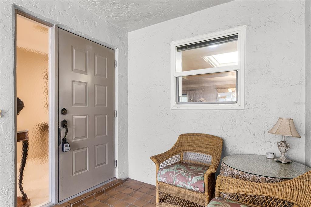 A covered entryway features a tan door, a window, and wicker furniture on tiled flooring — 5685 BADEN COURT, FORT MYERS, FL
