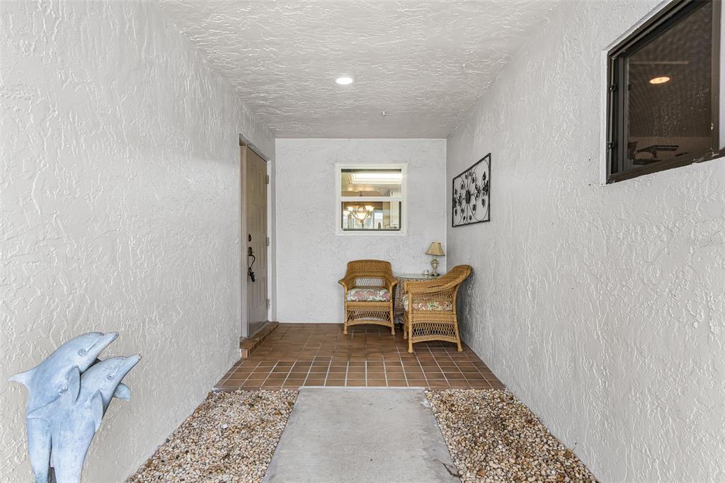 A covered entryway features a tiled floor, two wicker chairs, and a dolphin statue — 5685 BADEN COURT, FORT MYERS, FL
