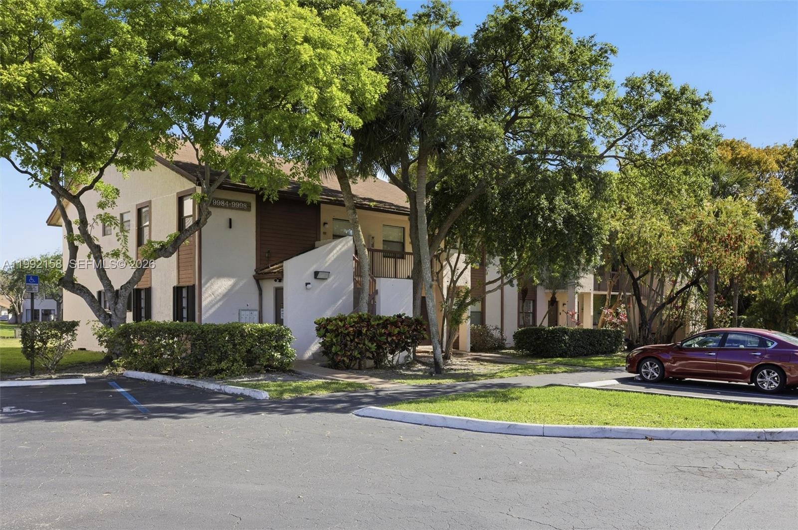 A two-story apartment building with beige stucco walls and brown wood accents sits outdoors — 9994 Nob Hill Ct # 9994, Sunrise FL 33351, SUNRISE, FL