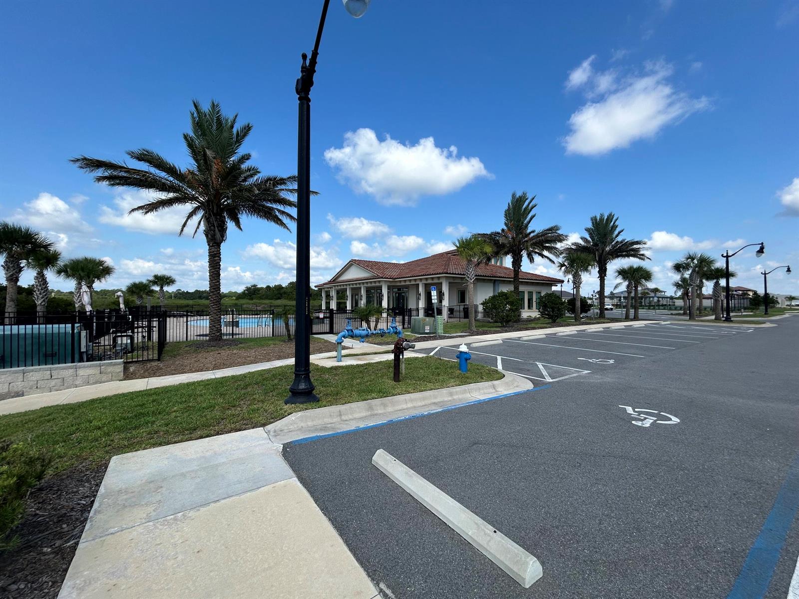 A parking lot with accessible spaces sits in front of a community building with palm trees — 24 Del Palma Drive, Palm Coast FL 32137, PALM COAST, FL