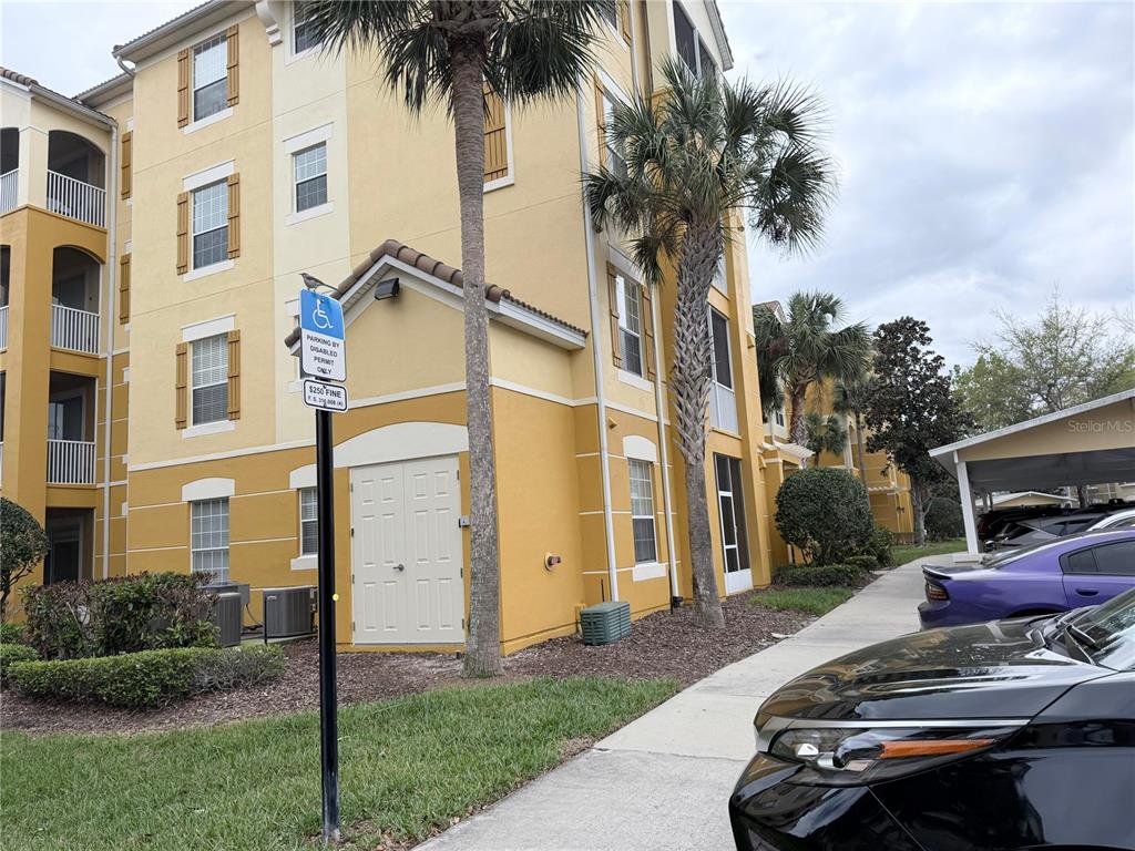 A multi-story yellow apartment building exterior features a handicap parking sign and a covered carport — 3338 ROBERT TRENT JONES DRIVE UNIT 20104, ORLANDO, FL