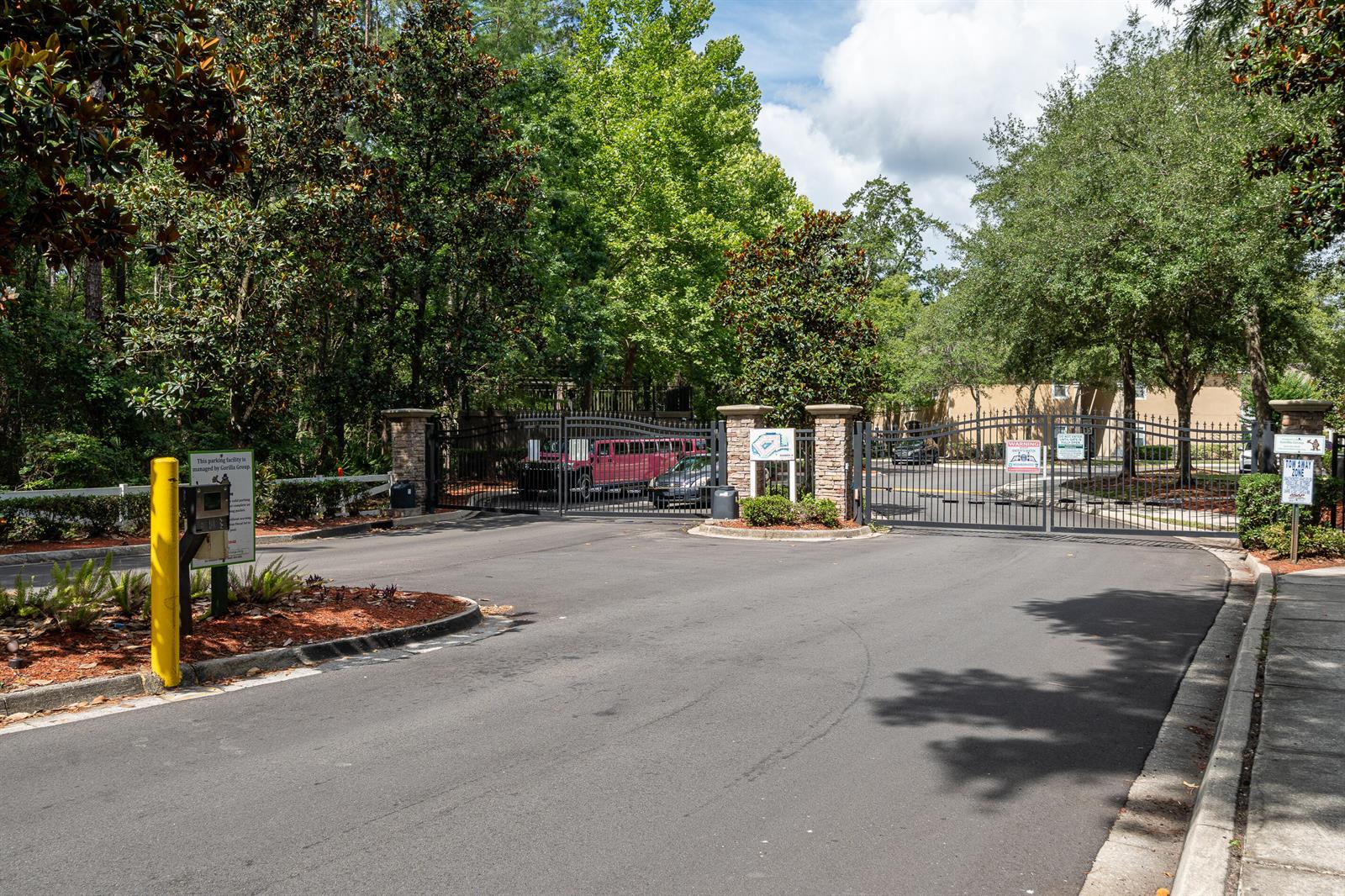 A gated entrance with stone pillars leads to a paved driveway surrounded by lush trees — 6069 Maggies Circle # 103, Jacksonville FL 32244, JACKSONVILLE, FL