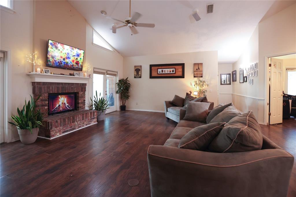 A living room features a brick fireplace, dark wood flooring, and a vaulted ceiling — 11923 LAKE BUTLER BOULEVARD, WINDERMERE, FL