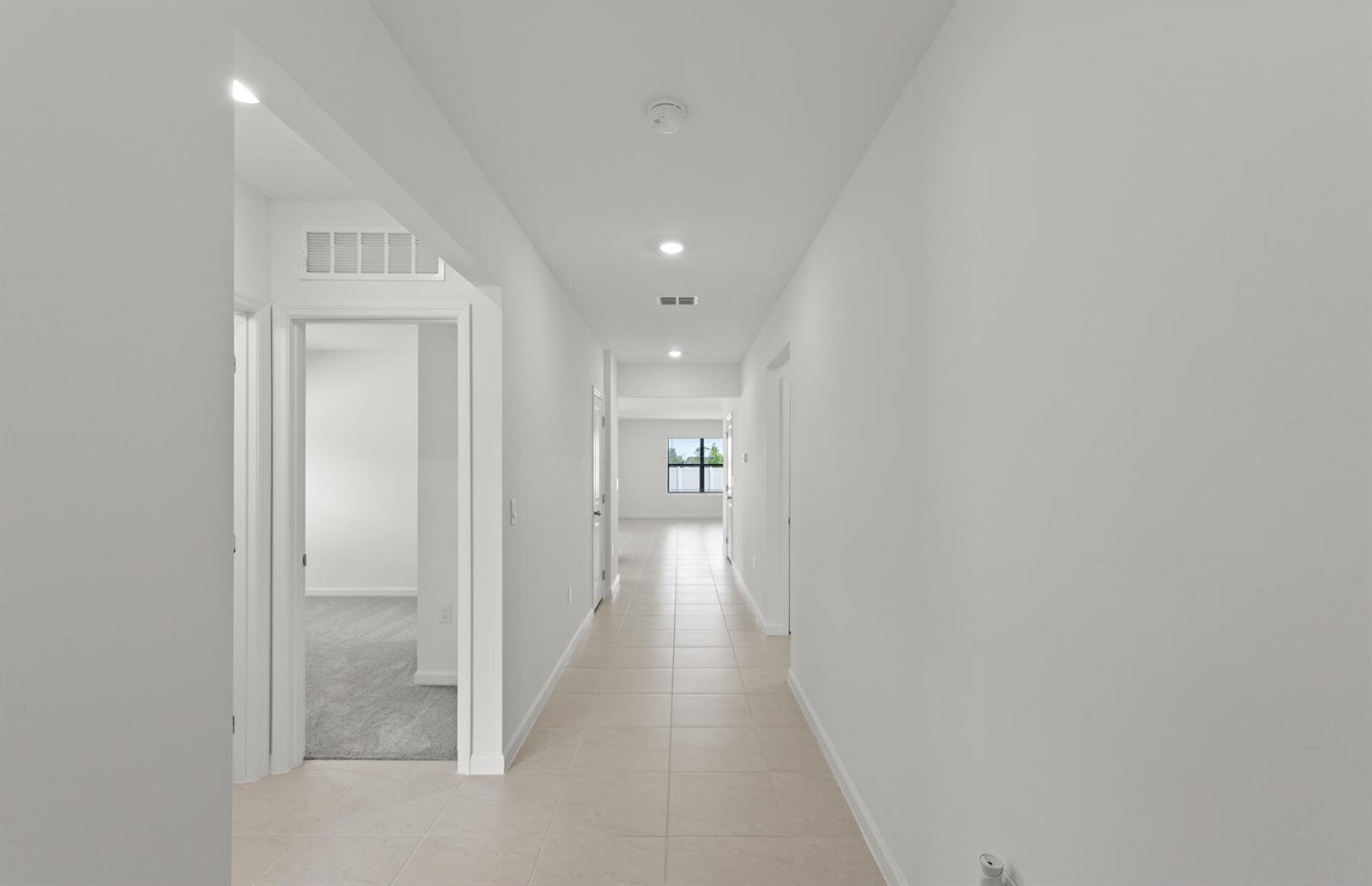 A long hallway with light-colored tile flooring leads toward a window at the far end — 1177 Caloosa Creek Drive, FL 33935, FL