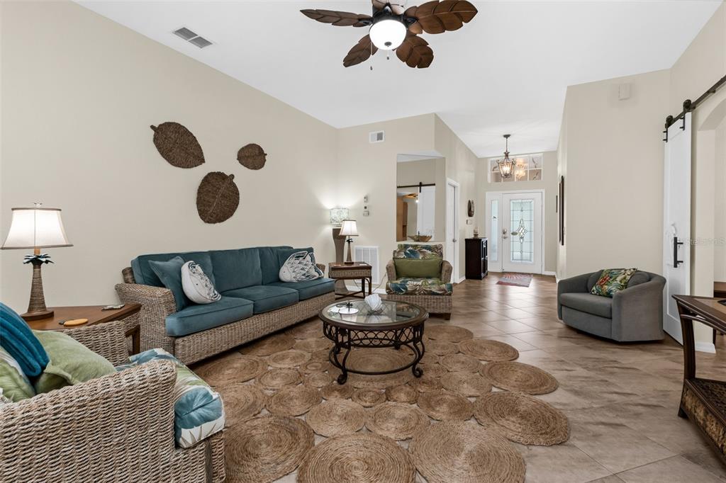 A living room features a blue sofa, wicker furniture, a round jute rug, and tile flooring — 1812 BIRMINGHAM BOULEVARD, PORT CHARLOTTE, FL