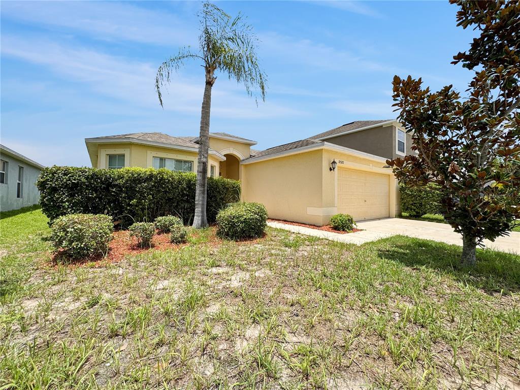 A single-story house with a yellow stucco exterior, a two-car garage, and a palm tree — 10520 STANDING STONE DRIVE, WIMAUMA, FL