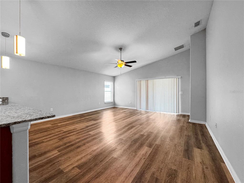 An empty living room features wood-look flooring, a ceiling fan, and sliding glass doors — 10520 STANDING STONE DRIVE, WIMAUMA, FL