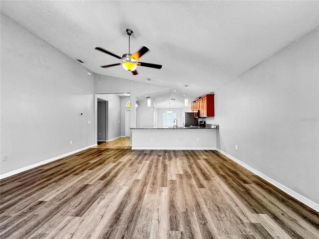 A spacious living room with wood-look flooring leads to an open kitchen with dark cabinets — 10520 STANDING STONE DRIVE, WIMAUMA, FL