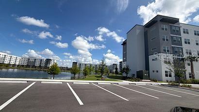 A parking lot sits in front of modern apartment buildings next to a small lake — 5587 MILLENIA PARK BOULEVARD UNIT 518, ORLANDO, FL