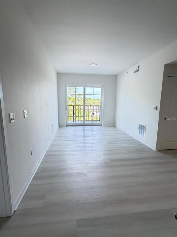 An empty room with light-colored wood-look flooring, white walls, and a sliding glass balcony door — 5587 MILLENIA PARK BOULEVARD UNIT 518, ORLANDO, FL