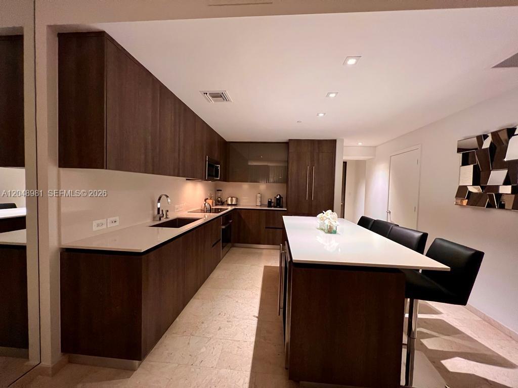 A modern kitchen features dark wood cabinetry, white countertops, a central island, and bar stools — 88 SW 7th St # 808, Miami FL 33130, MIAMI, FL