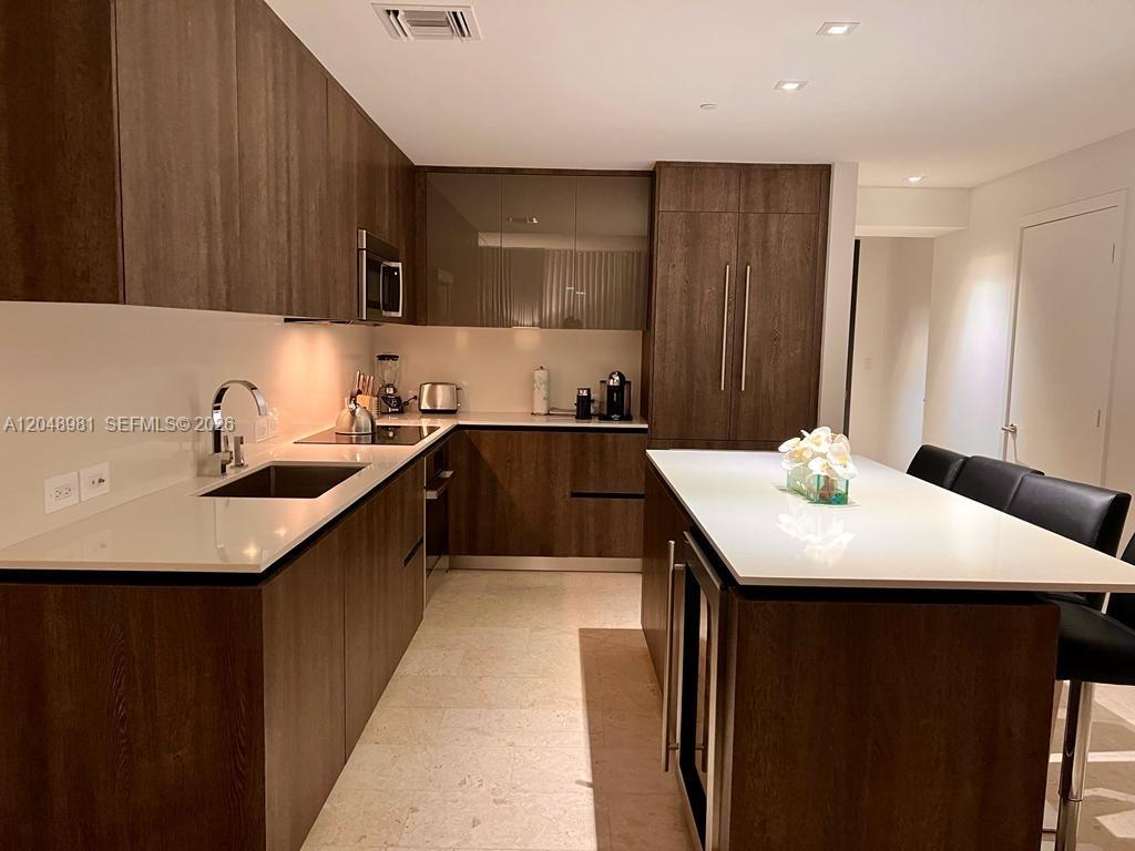 A modern kitchen features dark wood cabinetry, white countertops, a central island, and stainless steel appliances — 88 SW 7th St # 808, Miami FL 33130, MIAMI, FL