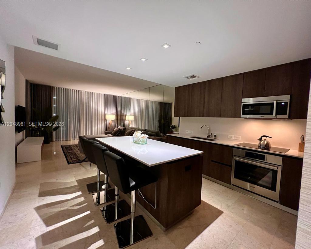 A modern kitchen features dark wood cabinetry, a white island with bar stools, and tile flooring — 88 SW 7th St # 808, Miami FL 33130, MIAMI, FL