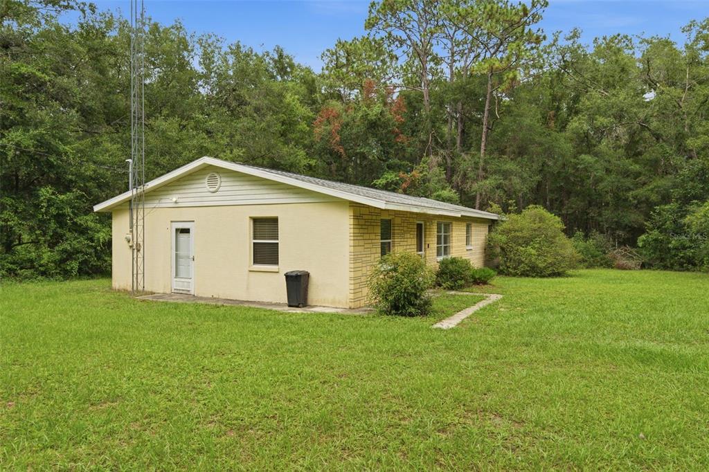 A yellow, single-story house with a brick accent wall stands on a grassy, wooded lot — 9955 S FORESTLINE AVENUE, INVERNESS, FL
