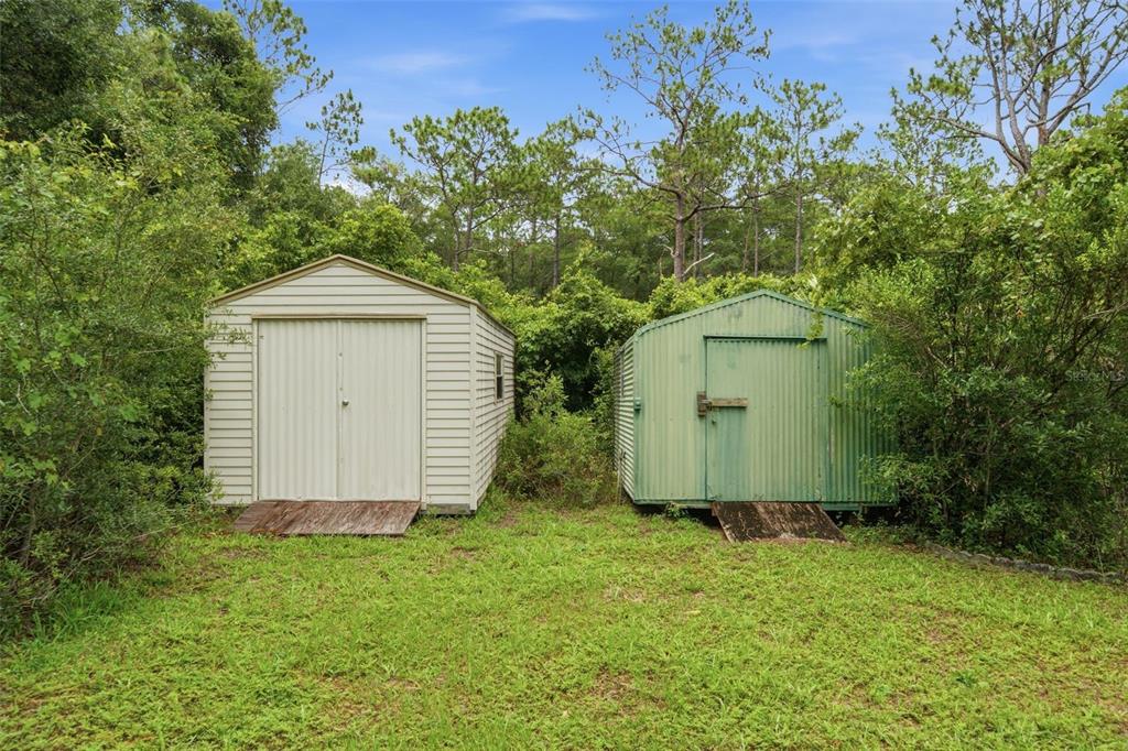 Two metal storage sheds sit on a grassy lawn surrounded by dense trees and foliage — 9955 S FORESTLINE AVENUE, INVERNESS, FL